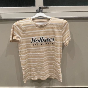 Randig t-shirt - Säljer en snygg beige och vit randig t-shirt från Hollister. Kortärmad och i mjukt materialet, mycket bra skick! 
