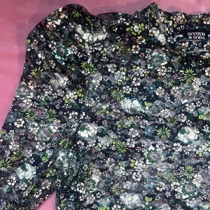 Blommig långärmad topp från Scotch & Soda - Snygg långärmad topp från Scotch & Soda med ett färgglatt blommönster i grönt, vitt och rosa. Perfekt för att liva upp garderoben med lite färg och mönster.Toppen är lätt transparent och har en liten puffärm.