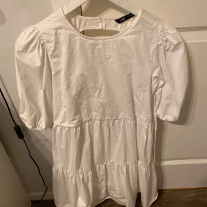 Vit klänning från Zara - Säljer en söt vit klänning från Zara med puffiga kortärmar och en öppen rygg. Klänningen har en knytning i ryggen och är perfekt för varma dagar. Den är tillverkad i ett lätt och luftigt material. Perfekt till studenten. Klänningen har använts 1 gång men med en liten fläck som syns på sista bilden, fläcken syns inte alls med klänningen på.