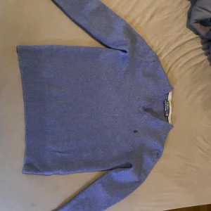 Blå tröja från Polo Ralph Lauren - Säljer en stilren blå tröja från Polo Ralph Lauren. Tröjan har en klassisk design med långa ärmar och ribbstickade muddar vid ärmslut och nederkant. Perfekt för en avslappnad men ändå elegant look.