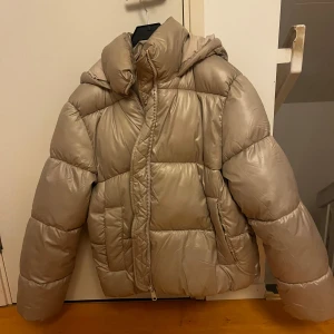 Beige pufferjacka med huva - Säljer en snygg beige pufferjacka med huva. Jackan har en dragkedja framtill och är quiltad för extra värme. Perfekt för kyliga dagar🩷