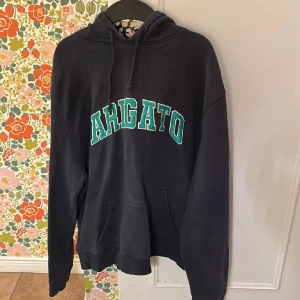 Svart hoodie från Axel Arigato - Snygg svart hoodie från Axel Arigato med grönt tryck på bröstet. Den har en klassisk design med huva och känguruficka framtill. Perfekt för en avslappnad stil.