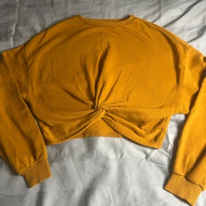 Gul croppad tröja från H&M Divided - Säljer en snygg gul croppad tröja från H&M Divided. Tröjan har långa ärmar och en knutdetalj framtill som ger en cool look. Perfekt för en avslappnad stil.