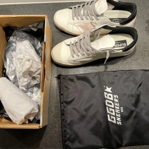 Vita sneakers från Golden Goose - Snygga vita sneakers från Golden Goose med grå snörning och en stjärndetalj i beige på sidan. Skorna har en svart häl och kommer med originalförpackning och påse.