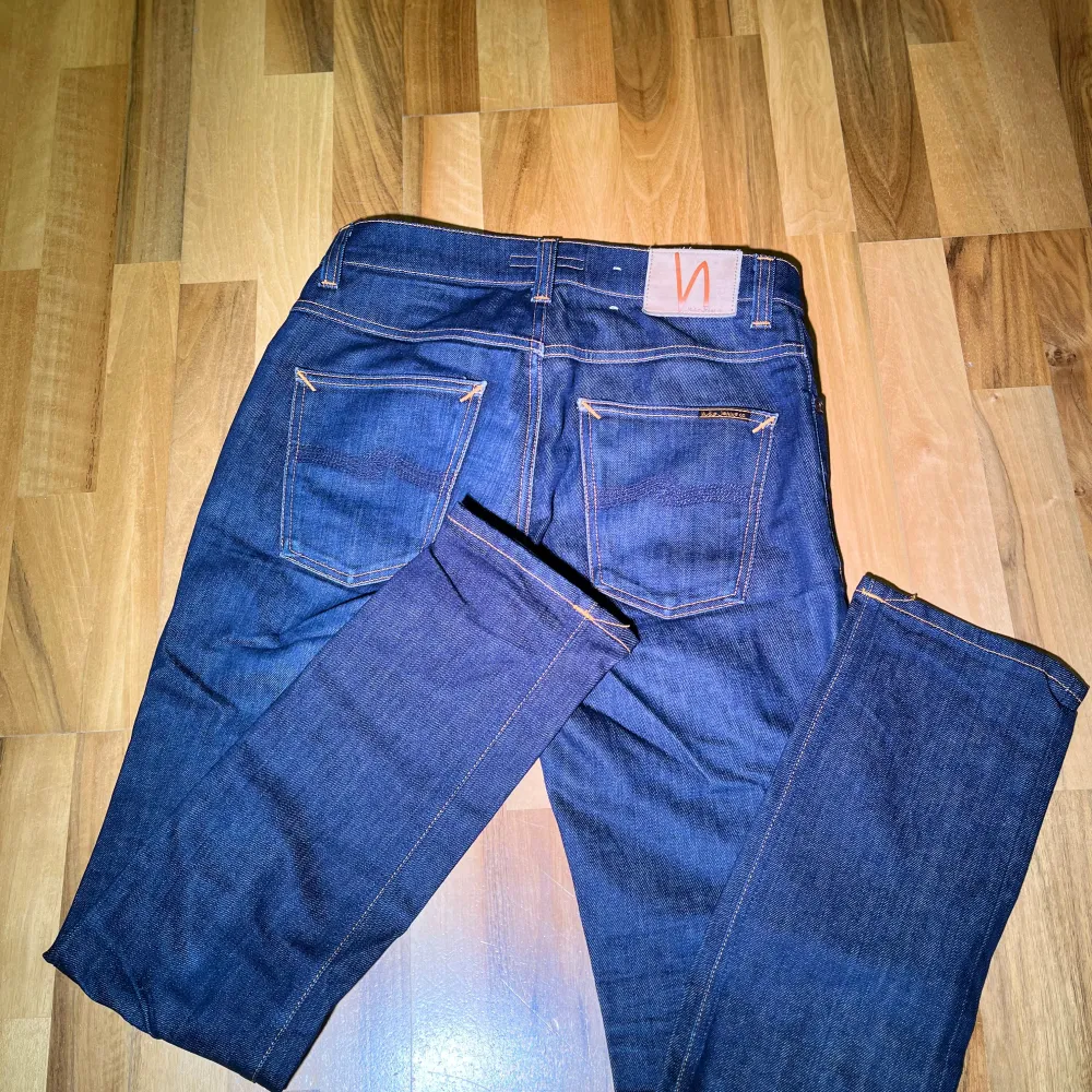 Säljer ett par mörkblå jeans från Nudie Jeans med klassisk femficksdesign och orange sömmar. Perfekta för en stilren look. Model: grim tim, storlek 31/32, finns små fläckar som ej syns på en distans. Farkut & Housut.