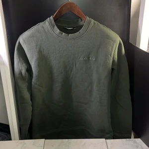 Grön tröja från J.Lindeberg - Säljer en stilren grön tröja från J.Lindeberg. Tröjan har en rund halsringning och är långärmad, perfekt för en avslappnad look. Diskret logga på bröstet ger en snygg touch. Hör av er vid minsta fundering🙌