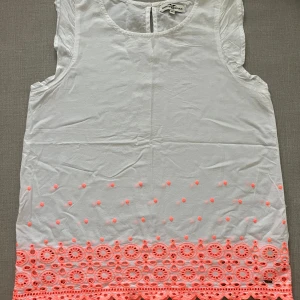 Vit ärmlös topp med neonrosa broderi - Säljer en söt vit ärmlös topp med neonrosa broderi och hålmönster längst ner. Perfekt för sommaren. 