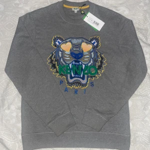 Grå sweatshirt från Kenzo - Säljer en grå sweatshirt från Kenzo jag säljer den för att den var för stor för mig, jag köpte den för 2700 men säljer den för 1300 den är aldrig använd, lapp finns kvar. Pris kan diskuteras. 