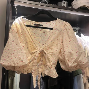 Blommig blus från Bik Bok - Söt blommig blus från Bik Bok i beige med små rosa blommor. Blusen har har en v-ring framtill samt knytning! 