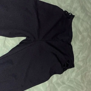 Svarta byxor med snörningsdetalj - Snygga svarta byxor från Fab med unik snörningsdetalj vid midjan. Byxorna har en elegant design och är perfekta för att ge en stilren look. De är tillverkade i ett mjukt och bekvämt material.