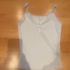Vit ribbad linnetopp med spetsdetaljer - Säljer en söt vit ribbad linnetopp med spetsdetaljer vid axelbanden. Tröjan är använd 1 gång. Toppen har knappar framtill och är perfekt för varma dagar eller under en kofta! Vet inte vart tröjan är ifrån men liknar den från Brandy Melville! Pris kan diskuteras och om du har en fråga eller vill ha fler bilder så får du jättegärna skriva, jag svarar snabbt!💕💕💗💗💗💗🫶🫶🫶🫶🫶