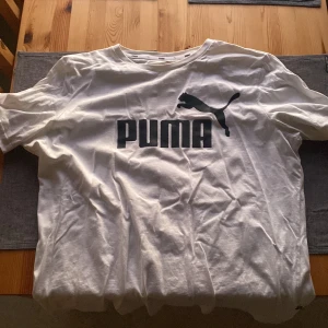 Vit t-shirt från Puma - Säljer en vit t-shirt från Puma med deras ikoniska logga i svart på bröstet. Perfekt för en avslappnad stil.