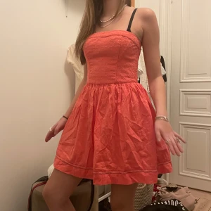 Rosa axelbandslös klänning - Trendig rosa/coral axelbandslös klänning med en kort och luftig design. Perfekt för sommarens varma dagar. Klänningen har en smickrande passform och en söt, feminin stil. 