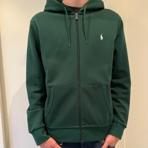 Ralph Lauren zip hoodie - Säljer en snygg grön zip hoodie från Ralph Lauren. Använd en handfull gånger - Skick: (9,8/10) - Mitt pris: 600kr - Nypris: 2400kr.  Modellen på bilden är 184cm