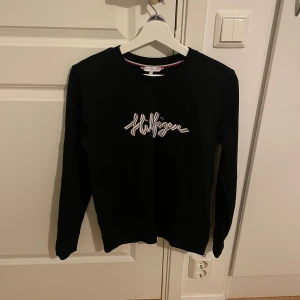 Svart tröja från Tommy Hilfiger - Säljer en stilren svart tröja från Tommy Hilfiger med deras logga i vitt på bröstet. Tröjan har långa ärmar och en klassisk rund halsringning. Perfekt för en avslappnad och trendig look. Den är använd fåtal gånger och är väldigt skön. För fler frågor och bilder så kan man kontakta mig privat🤍