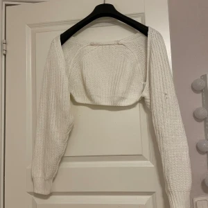 Vit stickad bolerotopp - Säljer en superfin vit stickad bolerotopp. Den är perfekt för att lägga till lite extra värme och stil till din outfit. Toppen har långa ärmar och en mysig, ribbad kant. Perfekt för höst och vår!, högra armen har en liten fläck,har ej tvättat,oanvänd