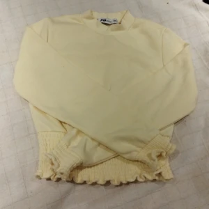 Gul tröja från FB Sister - Säljer en söt gul tröja från FB Sister i storlek XS. Den har långa ärmar och en ribbad kant vid ärmslut och nederkant som ger en fin volangeffekt. Perfekt för vår och sommar!