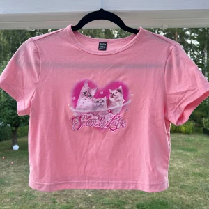 Croppad t-shirt med tryck - Croppad rosa t-shirt med gulligt katt-tryck 🐱💞 Aldrig använd så det är därför jag säljer den! Liten i storleken då jag själv bär S 🥰  (ALDRIG ANVÄND)  Längd: 44 cm Axel: 39 cm