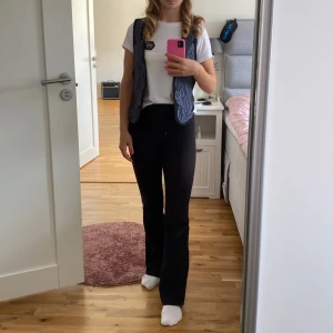 Svart väst med blå broderi - Säljer en snygg svart väst liknande Zara med coolt blått broderi på framsidan. Västen har en klassisk passform och knappar framtill. Perfekt för att ge din outfit en unik touch!