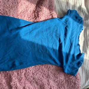 Blå ribbad klänning - Säljer en snygg blå ribbad klänning som är perfekt för sommaren. Den har korta ärmar och en tight passform som framhäver figuren. Klänningen är gjord av ett mjukt och stretchigt material, vilket gör den superbekväm att bära. Perfekt för både vardag och fest!