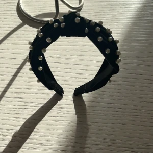 Svart diadem med pärlor - Säljer ett snyggt svart diadem dekorerat med vita pärlor. Perfekt för att ge en elegant touch till vilken outfit som helst. Diademet är brett och bekvämt att bära, och pärlorna ger en lyxig känsla. Passar både till vardags och fest!
