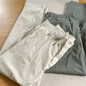 Beige och gröna byxor med dragsko - Säljer två par byxor från Hugo Boss. Ett par är beige och det andra är grönt. Båda har en avslappnad stil med dragsko i midjan för en bekväm passform. Perfekta för en casual look!