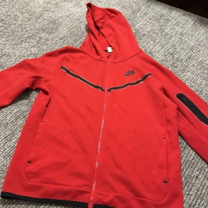 Röd hoodie från Nike - Säljer en snygg röd hoodie från Nike i storlek XL. Den har en dragkedja framtill och en huva för extra komfort. Perfekt för både träning och vardag. Den är i bra skick och redo för en ny ägare!