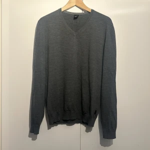 Grå tröja med v-ringning - Säljer en stilren grå tröja från Hugo Boss i storlek XL. Den har en klassisk v-ringning och är perfekt för både vardag och lite finare tillfällen. Tröjan är långärmad och gjord i ett mjukt material som känns skönt mot huden. Passar perfekt till höst och vinter!