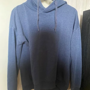 Blå hoodie - Säljer en snygg blå hoodie som är perfekt för både vardag och chill. Den har en klassisk design med dragsko i huvan och långa ärmar. Passar perfekt till jeans eller mjukisbyxor!
