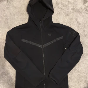 Nike Tech Fleece - Storlek Xs, använd och har ett pytte litet hål vid armen. Zippen har tappat lite färg.