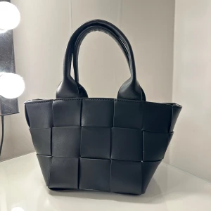 Väska braided pu bag - Söt och stilig väska från Gina tricot, använt en gång  Väskan är svart och har silverdetaljer. Den har lång, avtagbar axelrem och påsväska i linne inuti.