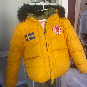 Gul dunjacka från Acne Studios - Säljer en gul dunjacka från Acne Studios X Fjällräven. Den har fluffig huva med svart päls. Jackan är perfekt för kalla vinterdagar med 100% dun. Den är helt oanvänd med etikett och har en lite oversized passform! Kontakta mig om du har fler frågor!💕
