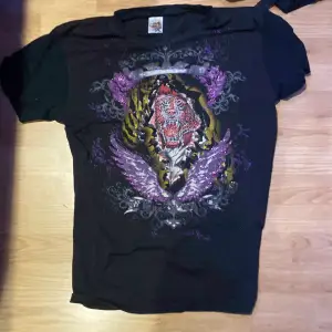 Säljer en svart t-shirt från Ed Hardy i storlek XL men passar mer som en Medium. Den har ett tryck av en tiger och vingar. Många små detaljer. Mycket bra skick!