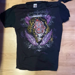 Svart ed hardy t-shirt med tigerdesign och paljetter - Säljer en svart t-shirt från Ed Hardy i storlek XL men passar mer som en Medium. Den har ett tryck av en tiger och vingar. Många små detaljer. Mycket bra skick!