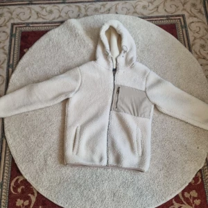 Vit teddyjacka från SMOG - Säljer en supermysig vit teddyjacka från SMOG i storlek S. Den har en praktisk dragkedja framtill och en cool ficka med dragkedja på bröstet. Perfekt för kyliga dagar med sin varma och gosiga känsla. Jackan har en huva med dragsko för extra skydd mot