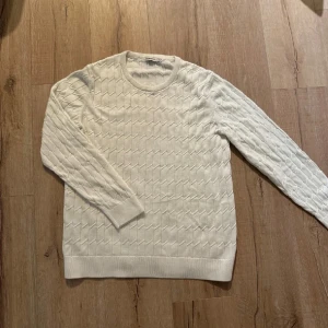Vit stickad tröja från J.Lindeberg - Säljer en snygg vit stickad tröja från J.Lindeberg. Den har ett coolt geometriskt mönster och är perfekt för både höst och vinter. Tröjan är långärmad och supermjuk, vilket gör den både stilren och bekväm. Perfekt för att hålla sig varm och trendig! 🤍