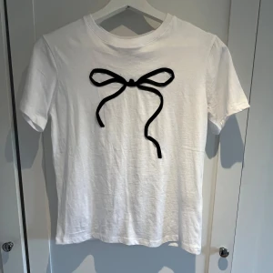  T-shirt med rosett - En vit t-shirt med en svart rosett från H&M. Stl xs. Aldrig använt. 