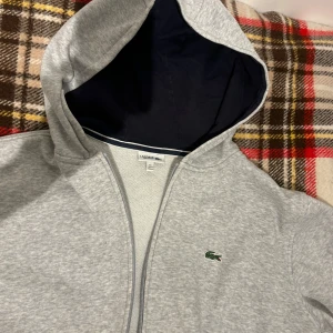 Lacoste zip hoodie  - En fin Lacoste zip up i bra skick. Skicka för fler bilder eller om du har frågor. Storlek 176 cm (XS) 