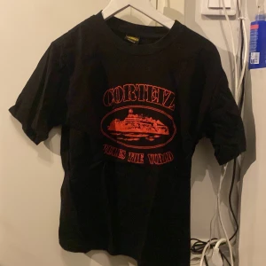 Svart t-shirt med rött tryck från Corteiz - Säljer en svart t-shirt från Corteiz med ett coolt rött tryck på framsidan. T-shirten har korta ärmar och en normal passform. Perfekt för en avslappnad stil.