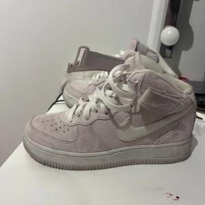 Nike Air Force i ljusrosa mocka - Snygga Nike Air Force i ljusrosa mocka med snörning och hög ankelrem. Perfekta för en stilren look med en touch av färg. Klassisk Nike-logga på sidan och bekväm sula.