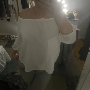 Vit offshoulder blus - Säljer en stilren vit offshoulder blus med trekvartsärmar. Perfekt för en avslappnad och chic look. Blusen har en luftig passform och är gjord i ett lätt material.