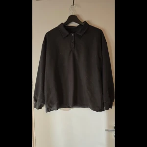 Svart långärmad pikétröja - Säljer en klassisk svart långärmad pikétröja med krage och knappar framtill. Hund finns i hemmet.