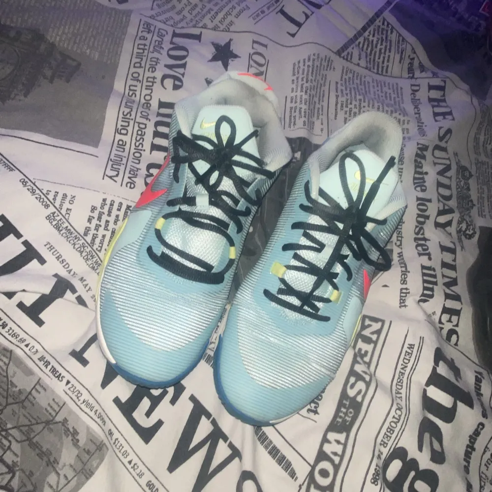 Snygga Nike sneakers i ljusblått med svarta snören och färgglada detaljer i rosa och gul. Skorna har en sportig design med en bekväm sula och är perfekta för en aktiv livsstil.. Kengät.