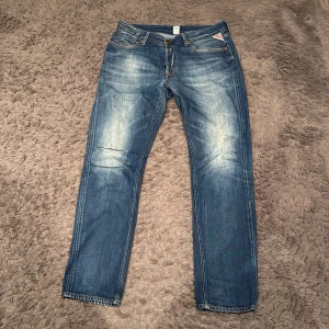 Blå jeans från Replay slim fit - Snygga blå jeans från Replay med en klassisk femficksdesign och slitna detaljer. De har en knappgylf och är perfekta för en avslappnad stil. Märkeslogga syns på bakfickan.                     Storlek W28 L28