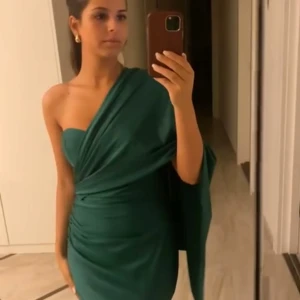 Grön axelbandslös långklänning - Elegant grön långklänning med en one-shoulder design. Klänningen har en draperad stil som ger en sofistikerad look. Perfekt för speciella tillfällen. Jättesnygg man kan ha den på flera sätt! använd en gång och köptes för 7000kr