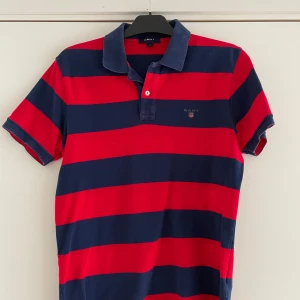 Randig pikétröja från GANT - Säljer en snygg randig pikétröja från GANT i rött och blått. 