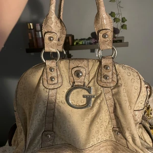 Beige handväska från Guess - Intressekoll på min guess väska❤️❤️ är sönder på insidan och användt rätt mycket💓 köpte den här på Plick .