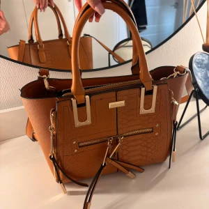 Brun väska  - Brun väska från river island med guld detaljer. Som ny! Stor får plats med mycket 