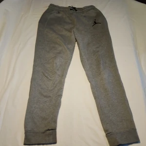 Grå mjukisbyxor från Jordan - Säljer ett par grå mjukisbyxor från Jordan med det klassiska Jumpman-logotypen på benet. Byxorna har en elastisk midja med snörning för justerbar passform och muddar vid bensluten. Perfekta för en avslappnad stil.