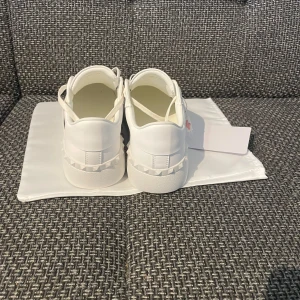 Valentino Garavani sneakers i vitt och svart - Snygga Valentino Garavani sneakers i vitt med svarta detaljer. Skorna har en klassisk design med snörning och de ikoniska nitarna på sidorna. Perfekta för en stilren look.storlek 42, skicka ett meddelande till mig om du har frågor!